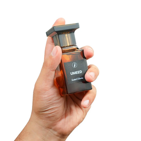 Hand holding a UMEED perfume bottle against a white background